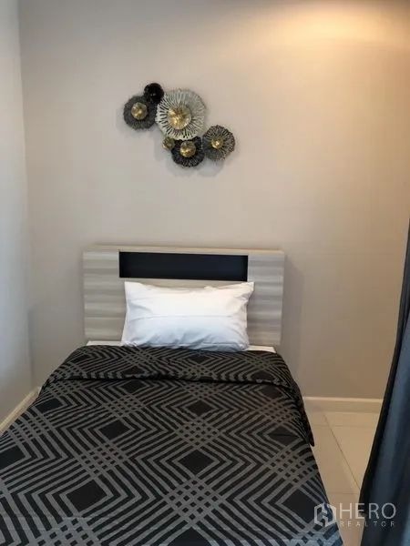 Condominium for rent in Watthana, Bangkok - Compact third bedroom with a single bed, geometric bedding, and decorative wall sculpture.