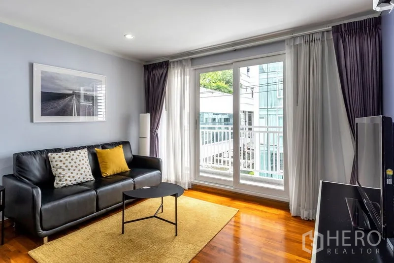คอนโด ให้เช่าในWatthana, Bangkok - ห้องนั่งเล่นโซฟาหนังสีดำ ประตูกระจกออกสู่ระเบียง พร้อมผ้าม่านเต็มบาน