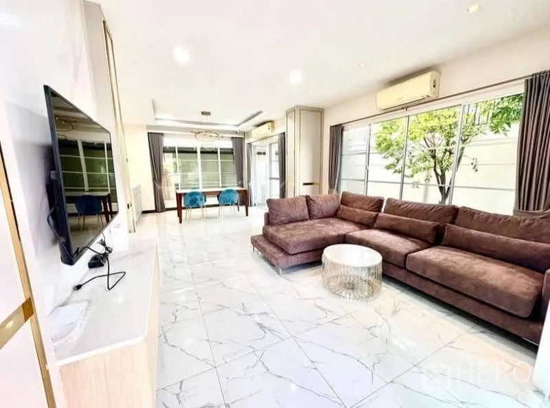 Detached House for rent in Phasi Charoen, Bangkok - Open-plan living room with L-shaped sofa, TV wall and full-height windows.