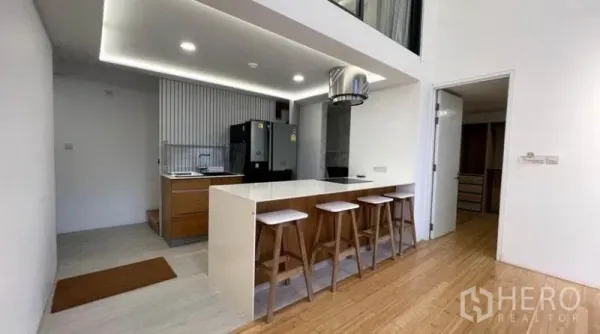 Condominium for rent in Watthana, Bangkok - Open-plan kitchen featuring a breakfast bar with four stools, double-door refrigerator, and cove lighting.