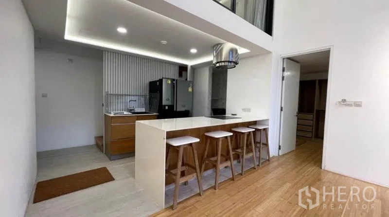 Condominium for rent in Watthana, Bangkok - Open-plan kitchen featuring a breakfast bar with four stools, double-door refrigerator, and cove lighting.