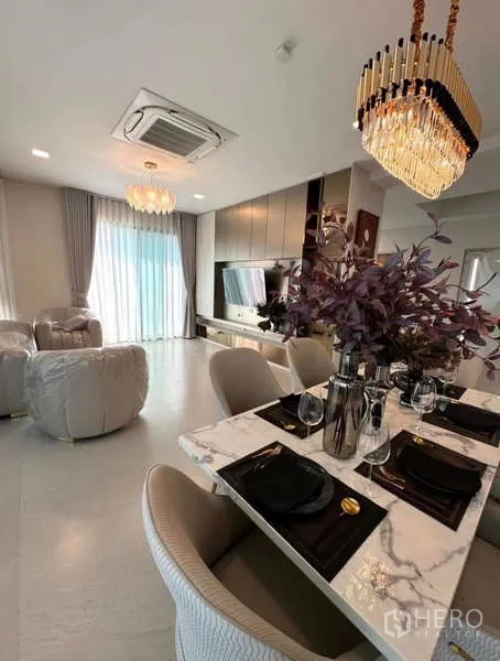 Detached House for rent in Samut Prakan - Open-plan dining and living area with chandelier and TV wall.