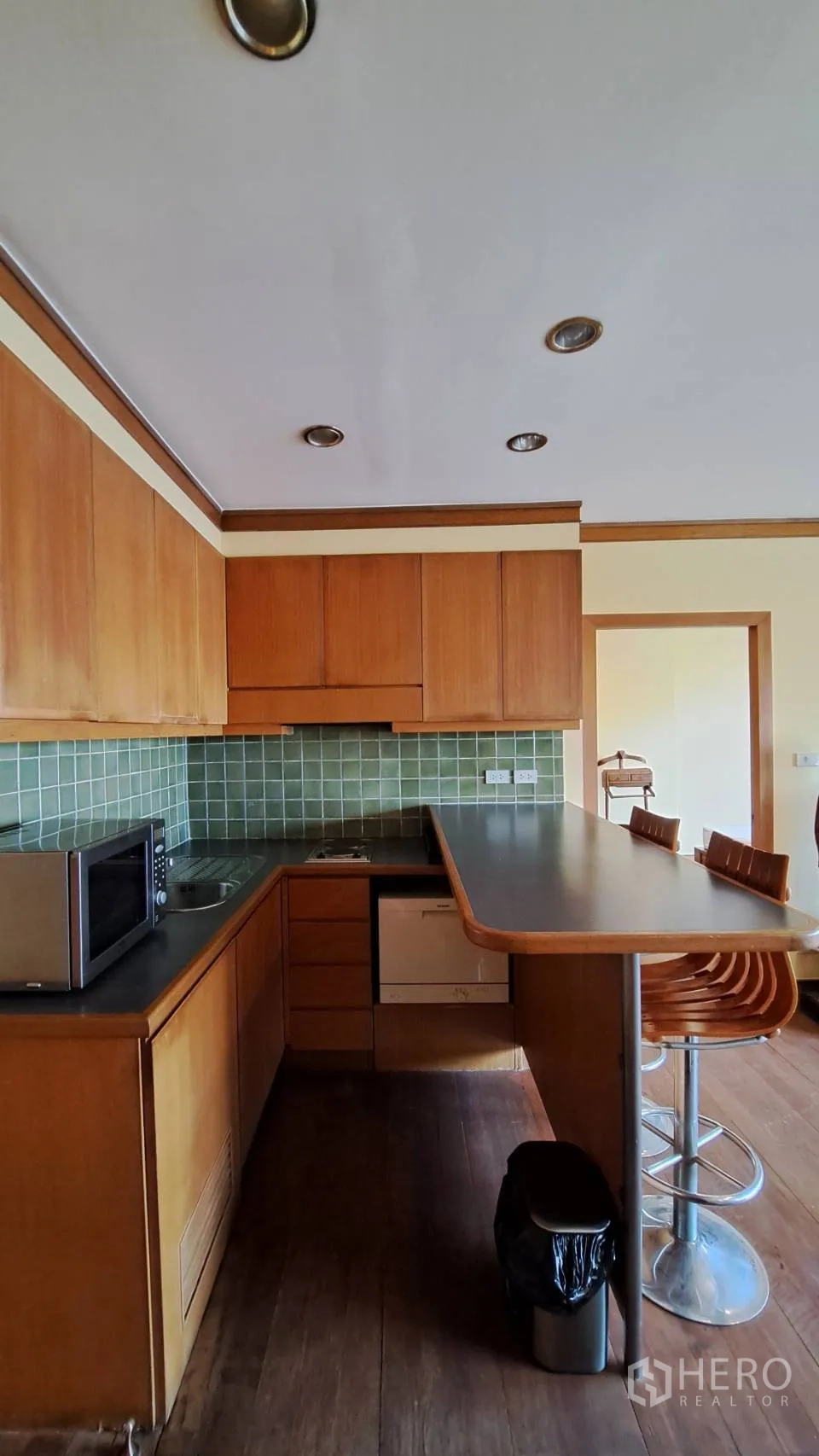 Condominium for rent in Khlong Toei, Bangkok - L-shaped kitchen with green tile backsplash, wood cabinetry, and breakfast bar.