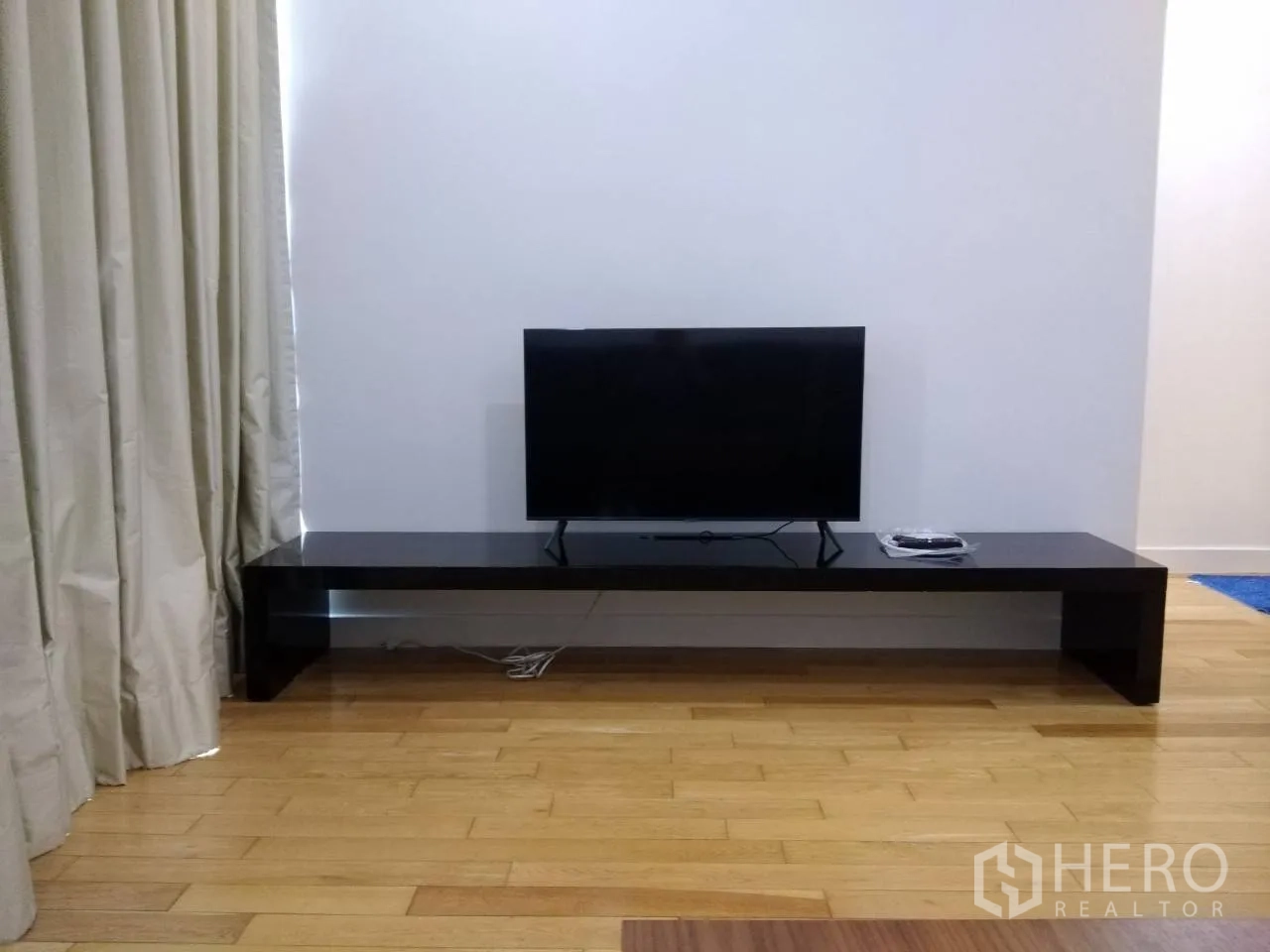 คอนโด ให้เช่าในKhlong Toei, Bangkok - ทีวีจอแบนบนชั้นวางเตี้ยสีดำข้างม่านยาวในห้องนั่งเล่น