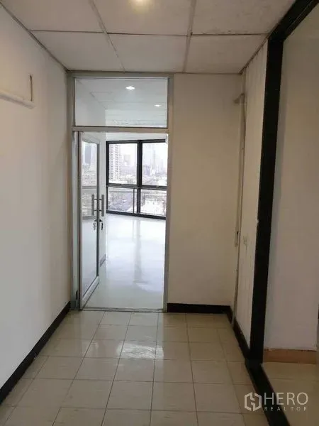 办公空间 出租在Bang Rak, Bangkok - 走廊通向带玻璃门的明亮办公室，可见城市景观。