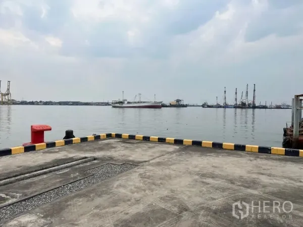 Warehouse for rent in Phra Samut Chedi, Samut Prakan - Private riverside quay with mooring bollard and cargo ships on the water.