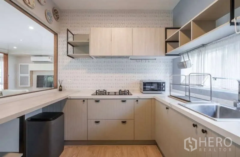 Detached House for rent in Prawet, Bangkok - Main U-shaped kitchen with gas cooktop, ample cabinetry and serving window to dining area.