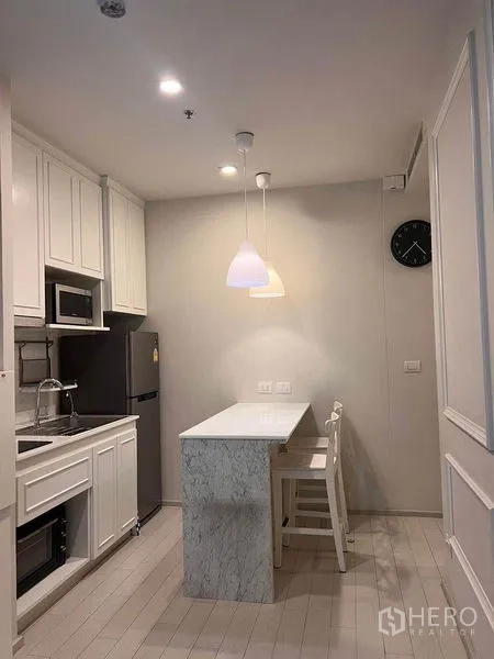 คอนโด ให้เช่าในPathum Wan, Bangkok - ครัวสีขาวพร้อมไอส์แลนด์หินอ่อน ไฟแขวน ตู้เย็นและไมโครเวฟ ในคอนโดปทุมวัน