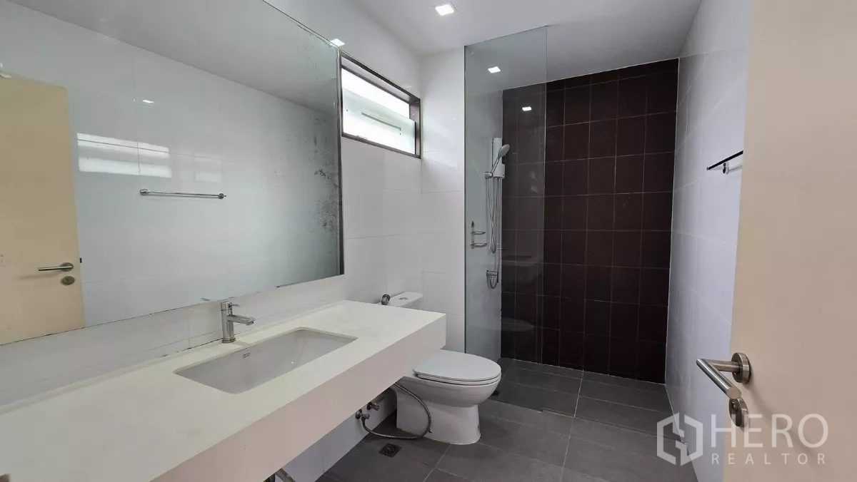 Townhouse for rent or sale in Saphan Sung, Bangkok - Bathroom featuring long countertop sink and dark-tiled walk-in shower.