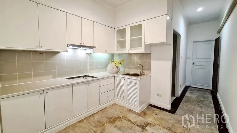 Condominium for rent in Watthana, Bangkok - White galley kitchen with cabinets, stovetop, and sink.
