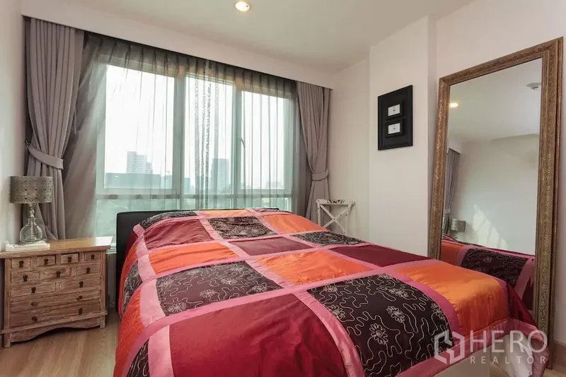 公寓 出租在Khlong Toei, Bangkok - 卧室采光好，落地窗、彩色被套、床头柜与全身镜。
