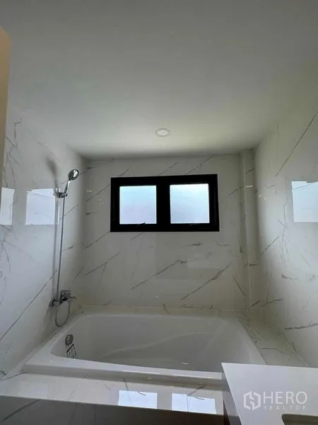 Detached House for rent in Don Mueang, Bangkok - Bathroom with white marble-look tiles, window and bathtub with shower.