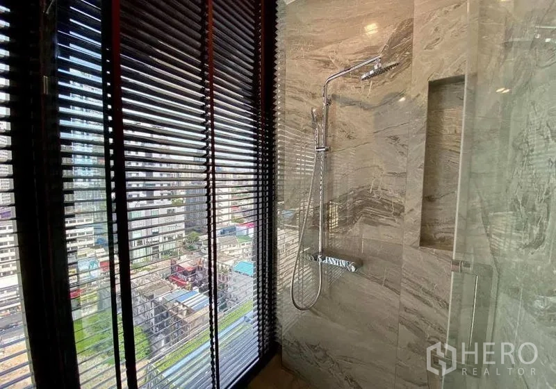 Condominium for rent in Watthana, Bangkok - Marble shower room with rainfall shower and window blinds overlooking the city.