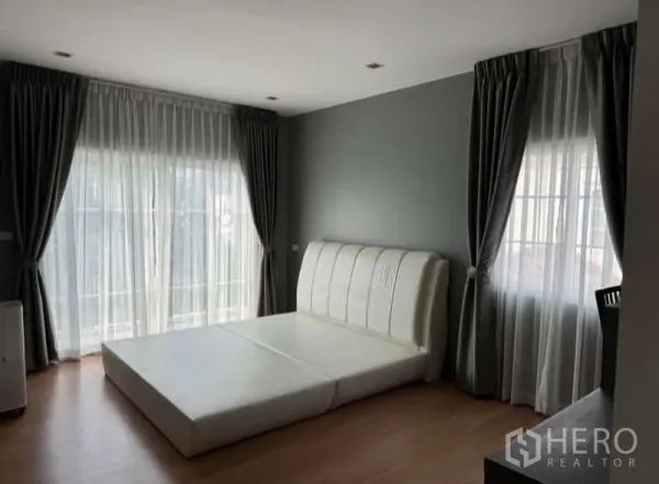 Detached House for rent in Bueng Kum, Bangkok - Master bedroom with large windows, sheer curtains and a padded bed base.