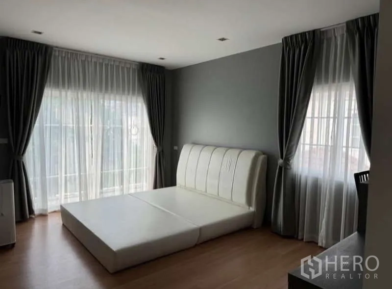 Detached House for rent in Bueng Kum, Bangkok - Master bedroom with large windows, sheer curtains and a padded bed base.
