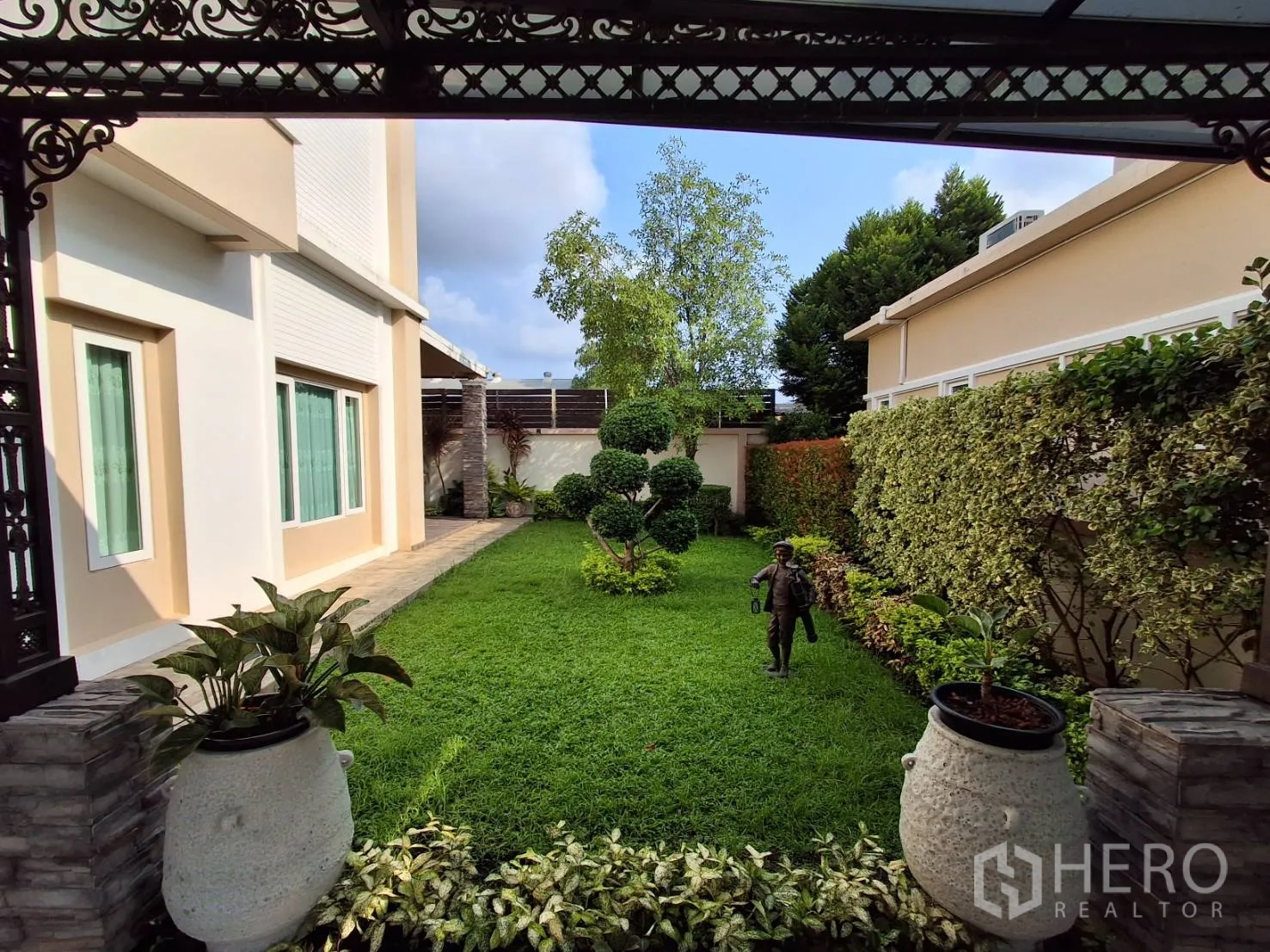 Detached House for rent or sale in Ban Chang, Rayong - Lush backyard lawn bordered by hedges and plants beneath a covered terrace.