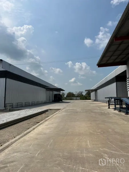 Warehouse for rent in Pathum Thani - Wide driveway between two steel-clad warehouses providing easy truck access.