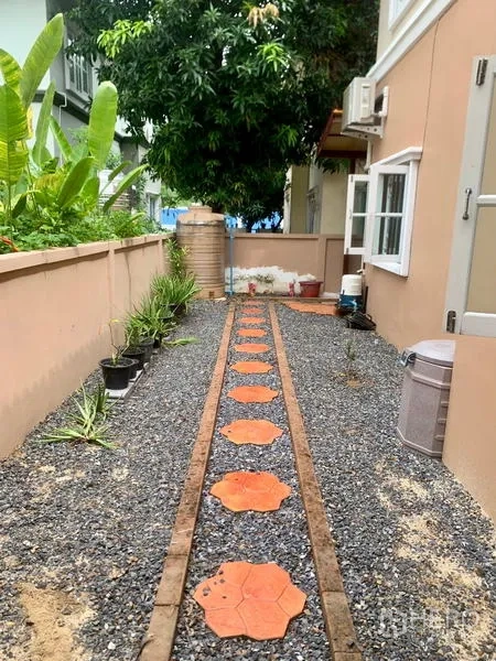 Detached House for rent in Khlong Sam Wa, Bangkok - Side garden with gravel path and terracotta stepping stones lined by potted plants.