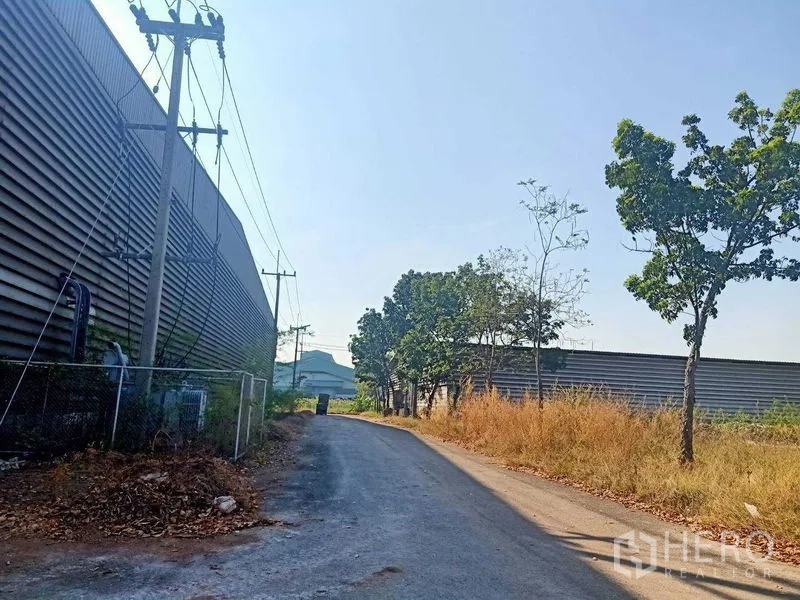 Warehouse for rent in Mueang Samut Sakhon, Samut Sakhon - Narrow industrial road with power poles and fencing along a warehouse exterior.