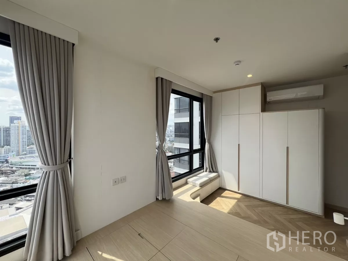 Condominium for rent or sale in Chatuchak, Bangkok - Sunlit bedroom with two corner windows, built‑in wardrobes and sweeping city views.