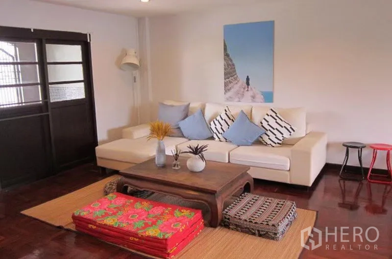 Townhouse for rent in Khlong Toei, Bangkok - Lounge area with cream sectional sofa, wooden coffee table and sliding doors.