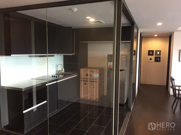 公寓 出租在Watthana, Bangkok - 封闭式玻璃厨房，深色橱柜与内置灶台，现代简约。