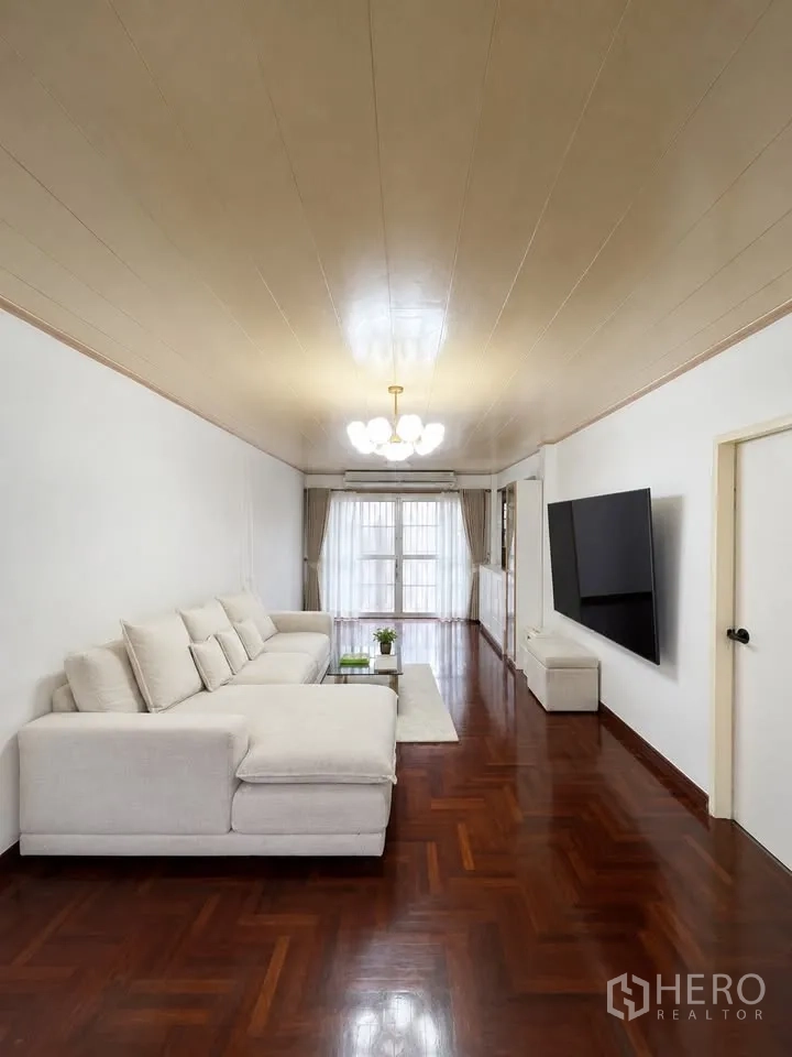 Detached House for rent in Prawet, Bangkok - Living room with large sectional sofa, wall-mounted TV and balcony doors.