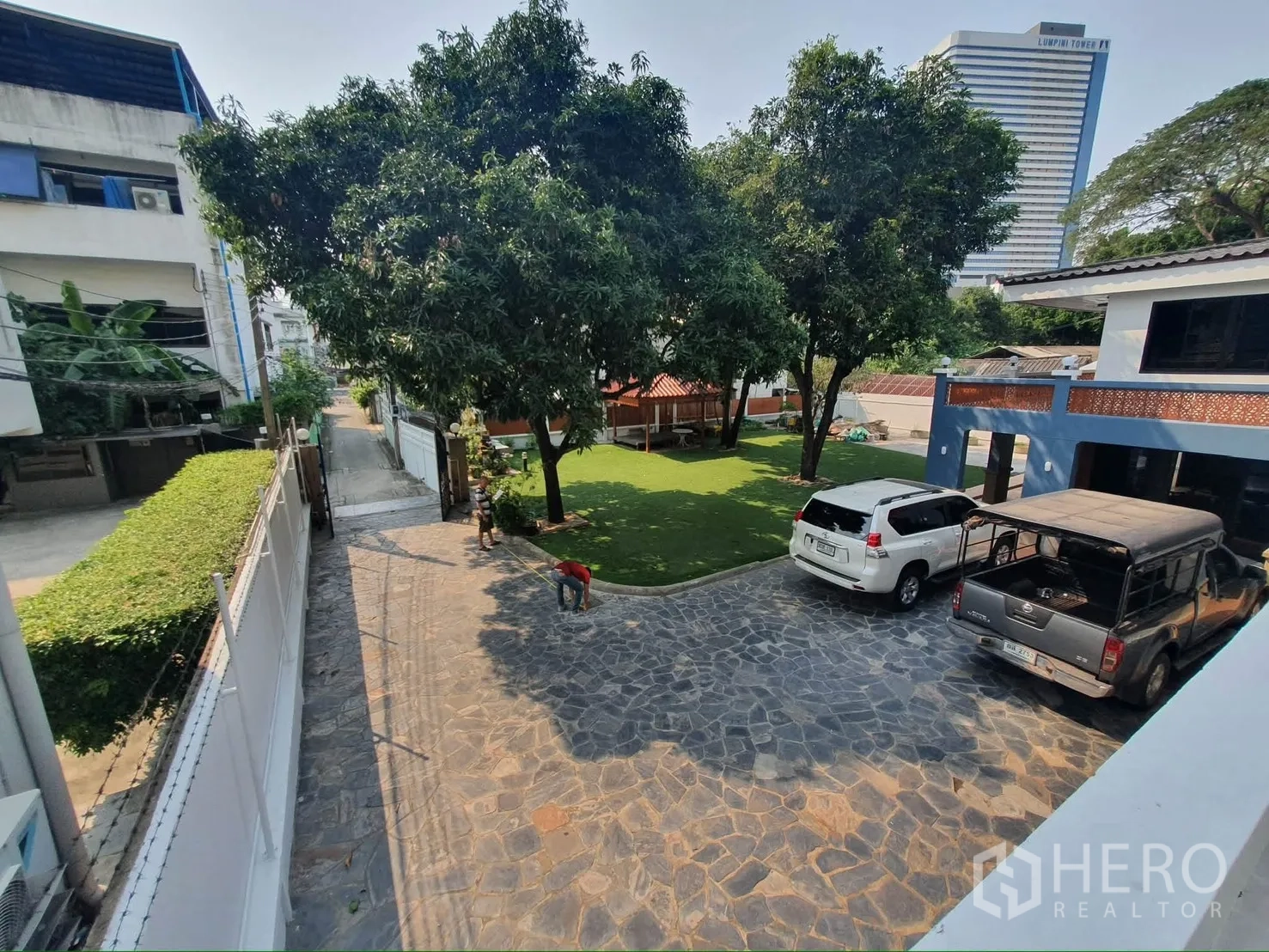 Detached House for rent in Sathon, Bangkok - Stone-paved driveway with gate, trees, and cars parked near the lawn.