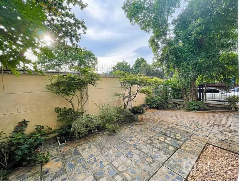 Townhouse for rent in Phasi Charoen, Bangkok - Paved courtyard garden with plants along a boundary wall and mature trees.