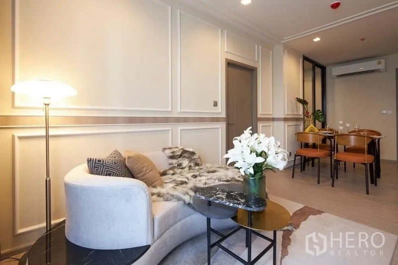 คอนโด ขายในRatchathewi, Bangkok - มุมนั่งเล่นโซฟาโค้งกับโคมไฟ ด้านหลังเป็นโต๊ะทานข้าว ผนังบัวคลาสสิก