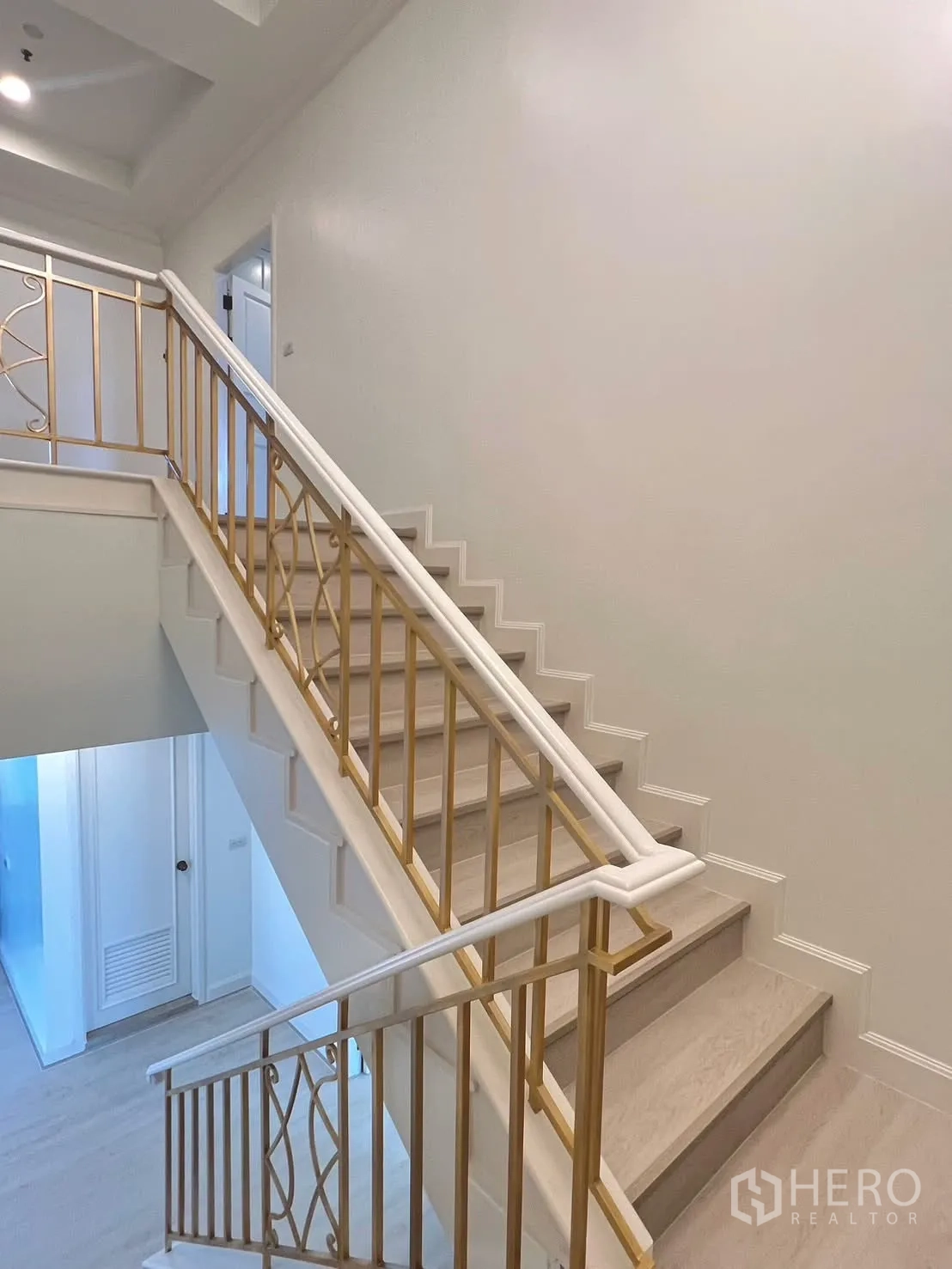 Condominium for rent in Khlong Toei, Bangkok - Interior staircase with gold-tone handrail and white walls.
