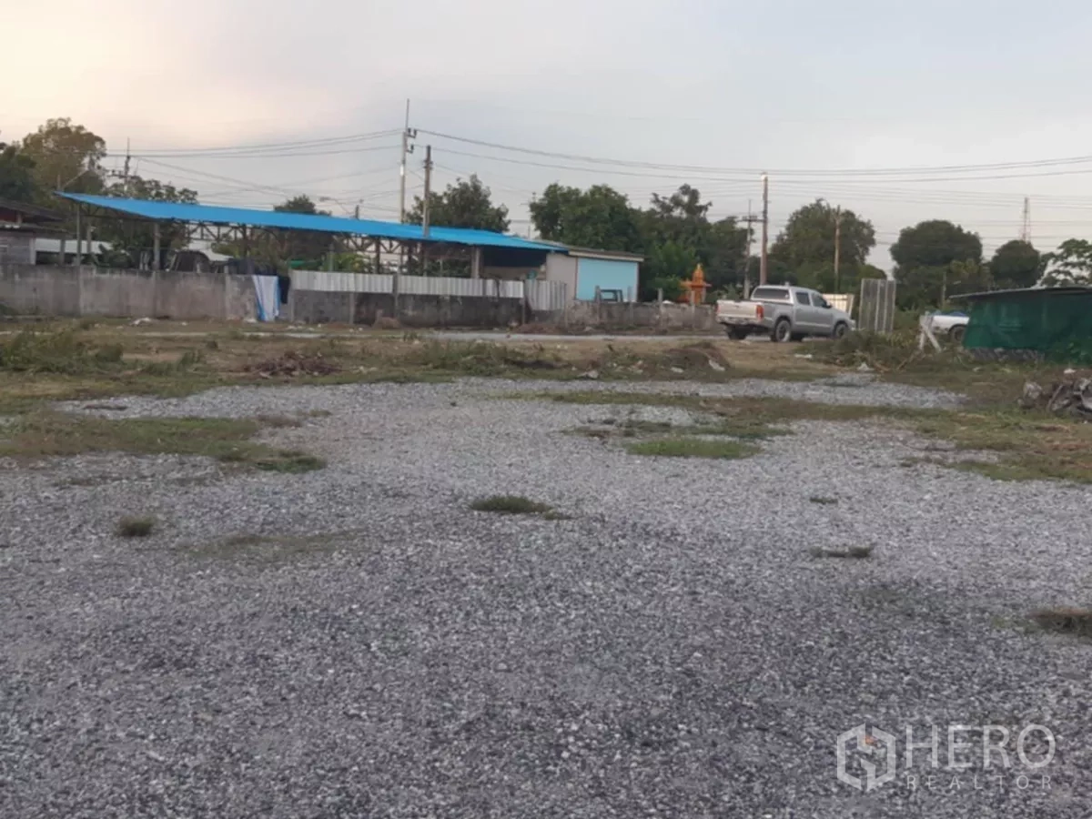 Land for sale in Khlong Toei, Bangkok - Leveled gravel land plot with boundary wall and access, vehicles in the background.