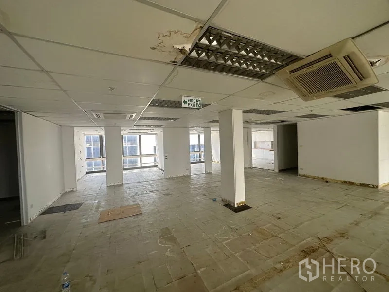 Office Space for rent in Khlong Toei, Bangkok - Partially fitted office space with columns, ceiling cassette air-conditioning and a fire-exit sign by large windows.