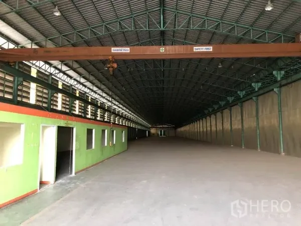 Warehouse for rent in Samut Prakan - Clear-span warehouse interior with high steel truss roof, internal office block along one side, concrete floor, and overhead crane beam.