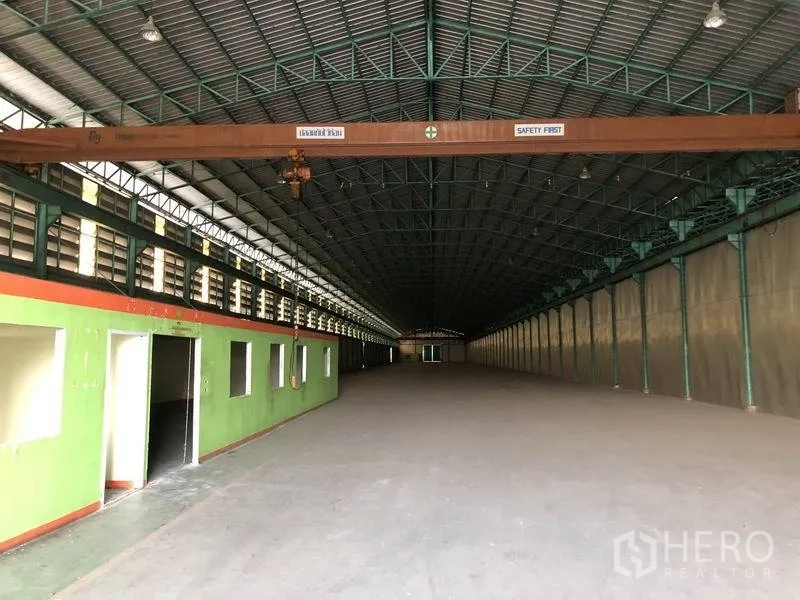 Warehouse for rent in Samut Prakan - Clear-span warehouse interior with high steel truss roof, internal office block along one side, concrete floor, and overhead crane beam.