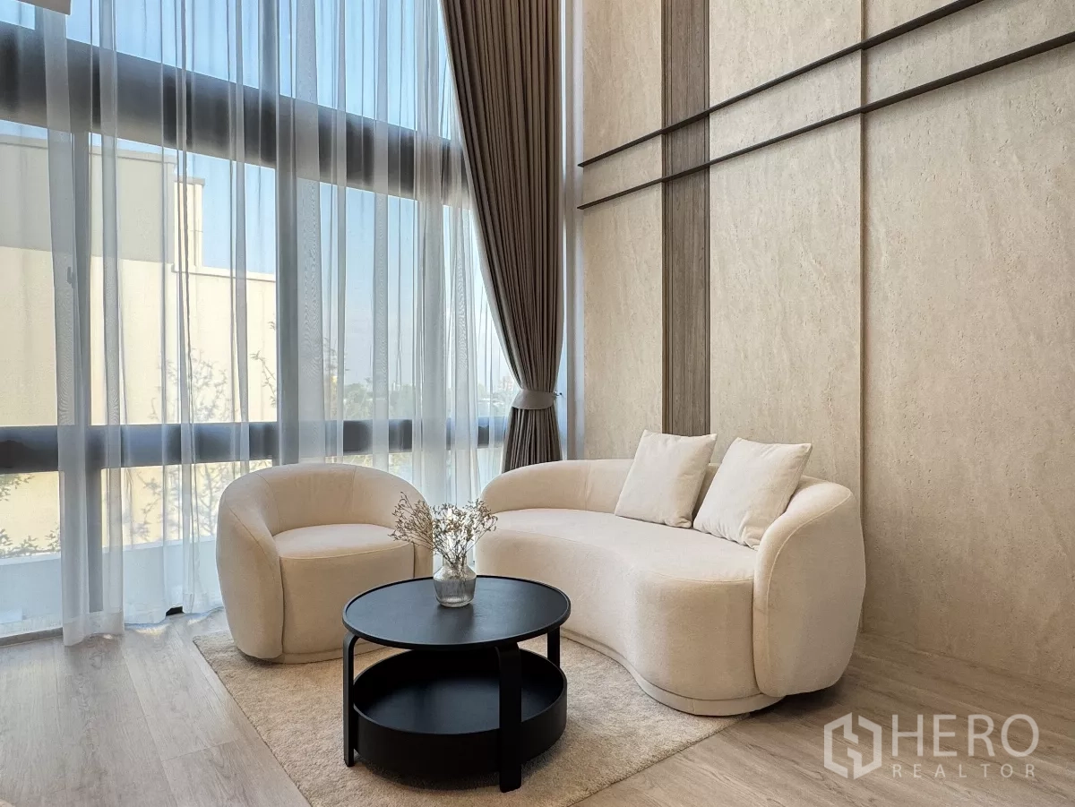 Detached House for rent in Saphan Sung, Bangkok - Cozy sitting area with curved sofa and armchair beside double-height windows with sheer drapes.