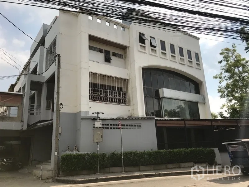 สำนักงานที่บ้าน ให้เช่าในPhra Khanong, Bangkok - อาคารโฮมออฟฟิศสีขาวหลายชั้น พร้อมกระจกโค้งบานใหญ่ โรงจอดรถมีประตูรั้ว และพุ่มไม้ริมถนนเงียบสงบ
