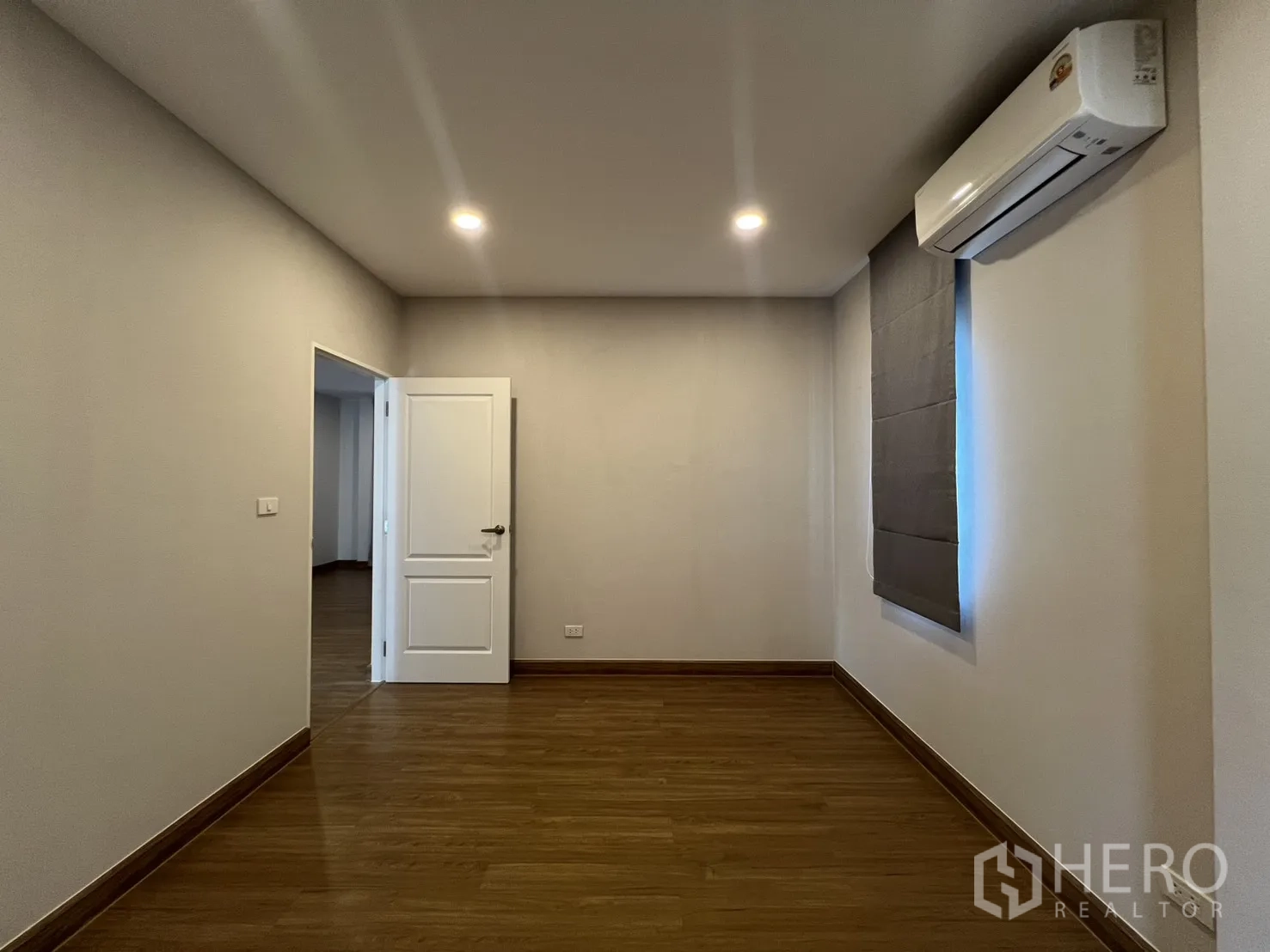 Detached House for rent in Lat Krabang, Bangkok - Simple bedroom with wood floor, recessed lights, air conditioner, and window blind.