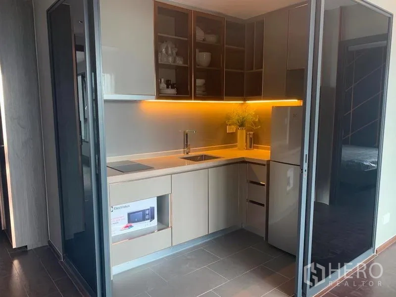 Condominium for rent in Watthana, Bangkok - L-shaped kitchen with under-cabinet lighting, electric hob, fridge and open shelving.