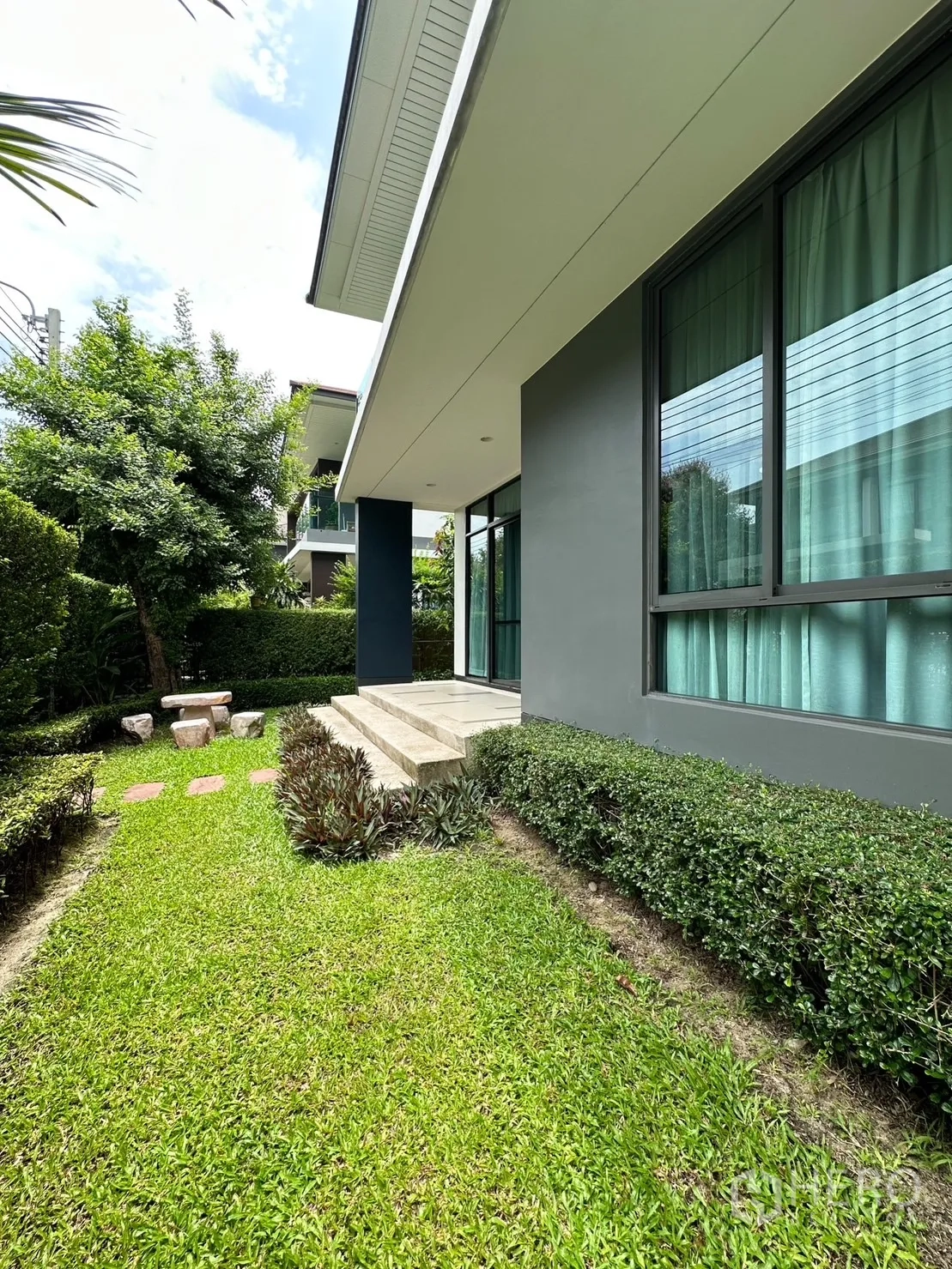 Detached House for rent or sale in Bang Kapi, Bangkok - Side of the house showing large windows, patio steps and landscaped lawn.
