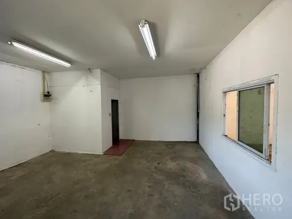 Warehouse for rent in Bang Bo, Samut Prakan - Simple internal office room with window, fluorescent lights, and concrete flooring.