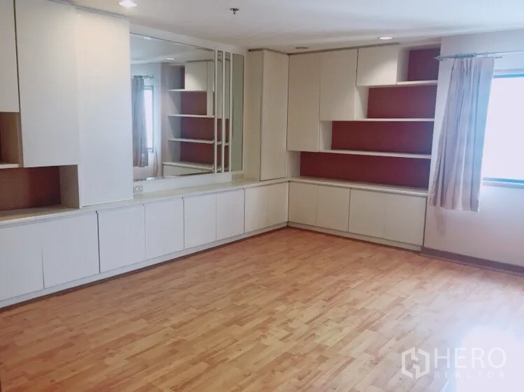 Condominium for rent in Watthana, Bangkok - Bright living room with built-in white cabinets, wall mirror, wood flooring and window in a Watthana condo.