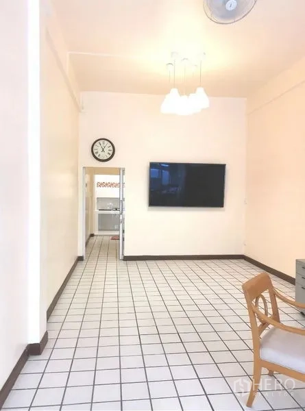 Townhouse for rent in Watthana, Bangkok - Ground-floor living space with white tile flooring, wall-mounted TV, ceiling lights, and doorway to kitchen.