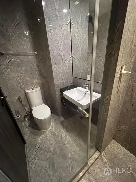 Condominium for rent in Watthana, Bangkok - Contemporary bathroom with glass shower, toilet, and wall-mounted basin in gray stone.