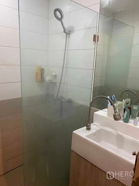 Condominium for sale in Bang Rak, Bangkok - Modern bathroom with glass shower enclosure, white basin and tiled walls.