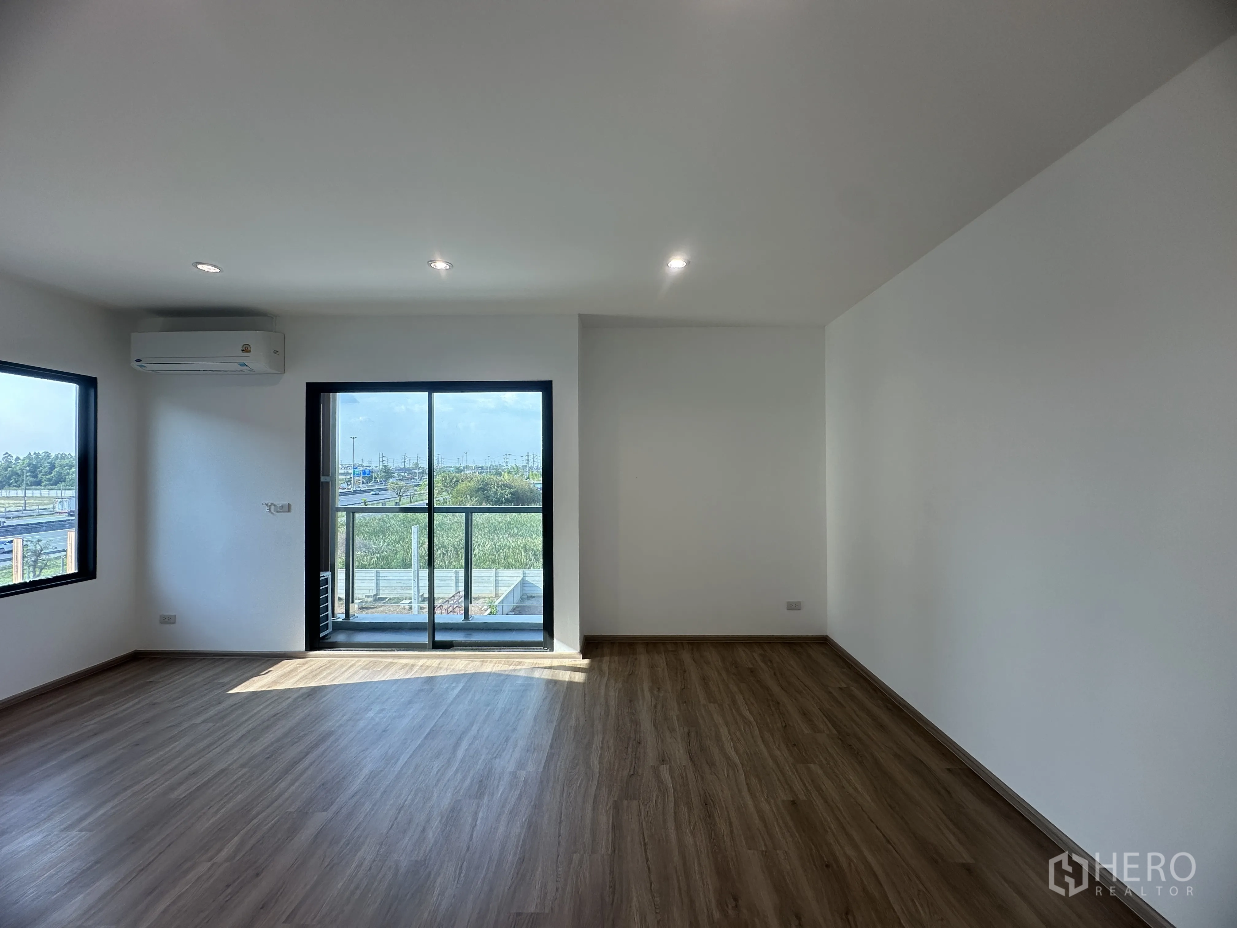 Home Office for sale in Khlong Luang, Pathum Thani - Corner bedroom or office with wood floors, air conditioner, and balcony overlooking greenery.