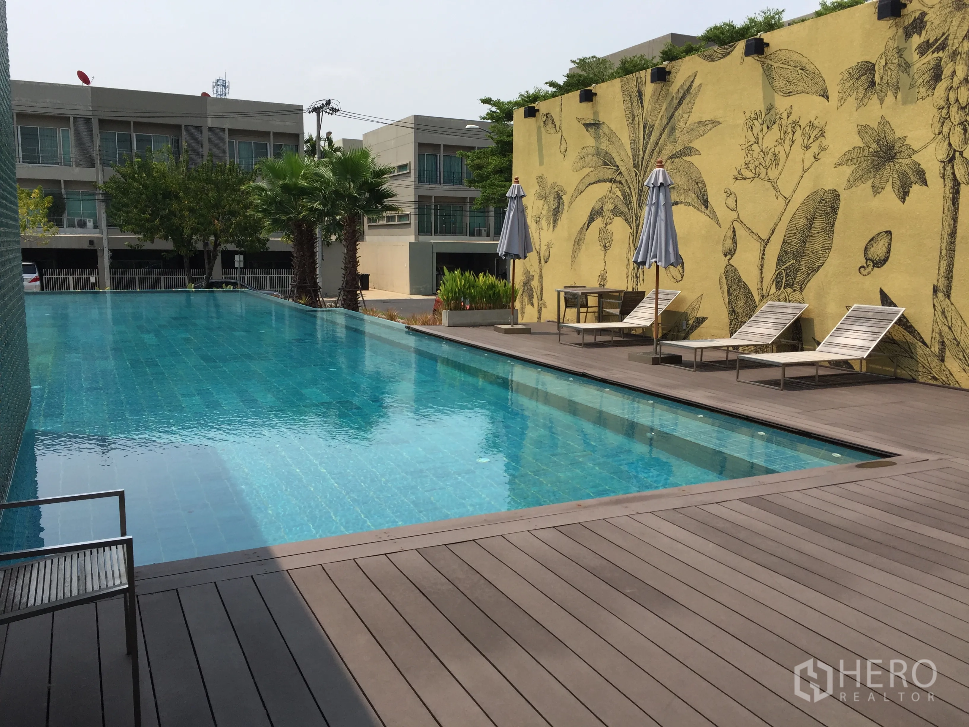 ทาวน์เฮาส์ ขายในSuan Luang, Bangkok - สระว่ายน้ำกลางแจ้งพร้อมเตียงอาบแดด ต้นปาล์ม และผนังลายพฤกษา