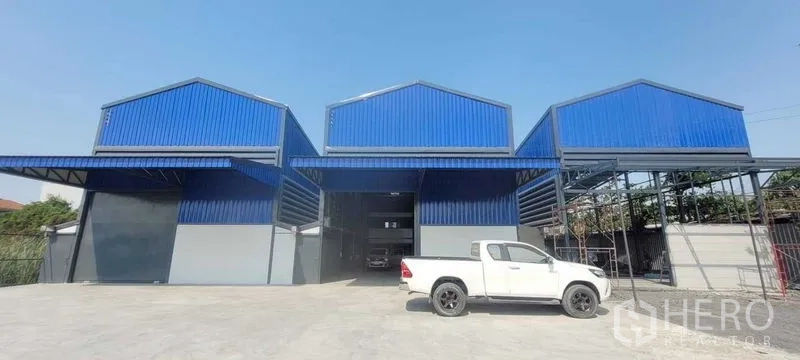 Warehouse for rent in Prawet, Bangkok - Blue steel-clad warehouse complex with wide concrete yard and parking at the front.