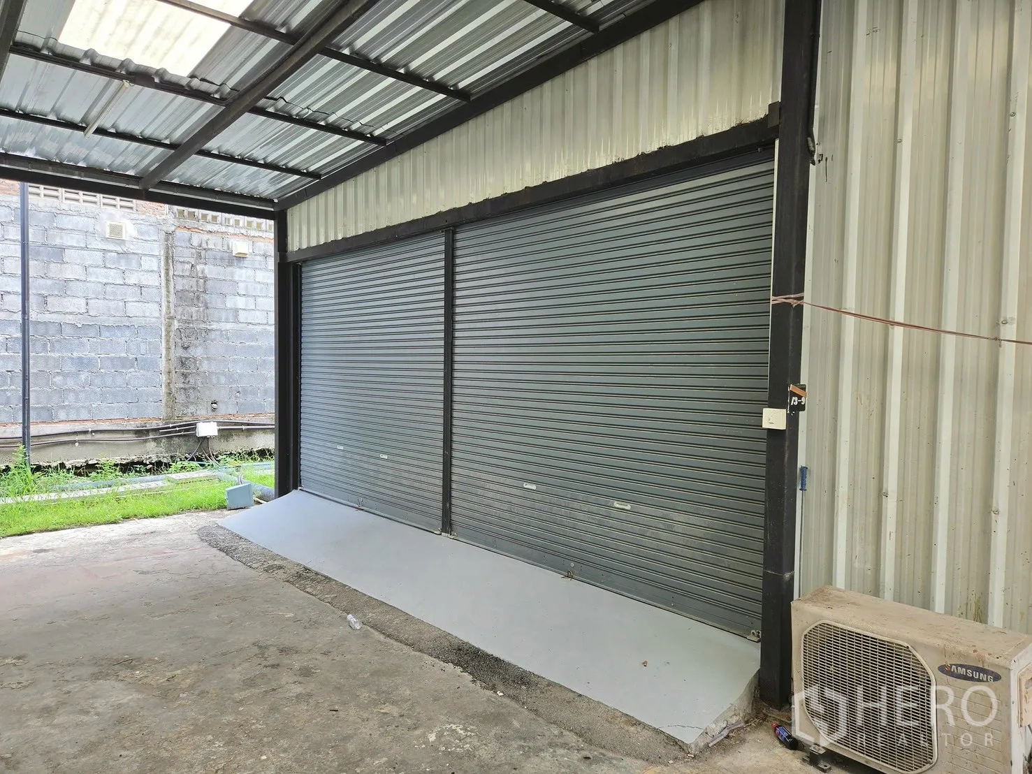 Warehouse for rent in Suan Luang, Bangkok - Covered loading bay with twin roller shutter doors and a small ramp.