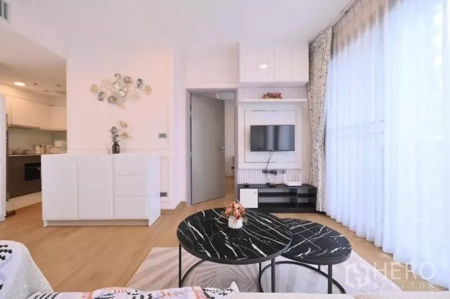 Condominium for rent in Watthana, Bangkok - Bright living room with round black marble coffee tables, TV wall and floor‑to‑ceiling sheer curtains.